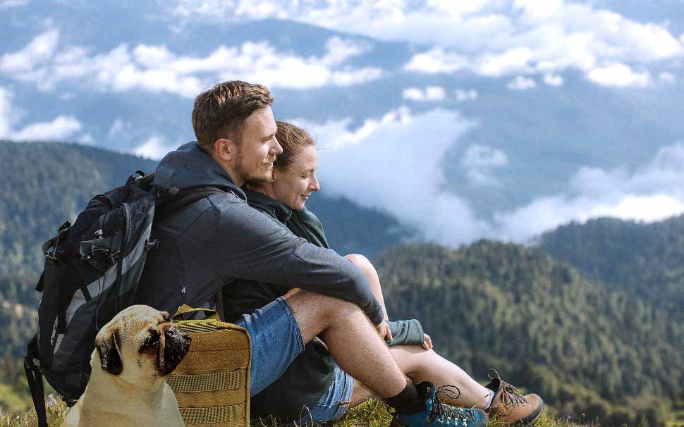 Couple and dog hiking in mountains with pet kit