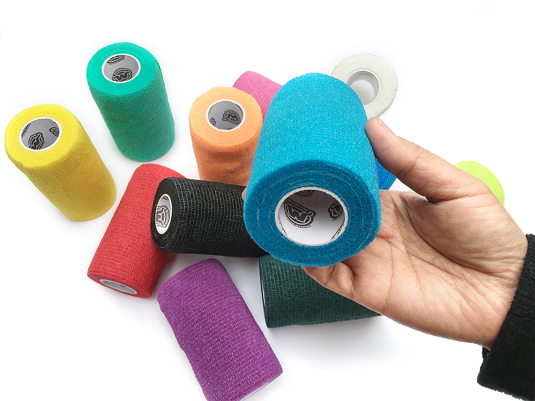 Hand Holding Roll of WildCow Multicolored Vet Wrap with Remaining Rolls in Background - 12 Color Pack, 4 Inches X 5 Yards